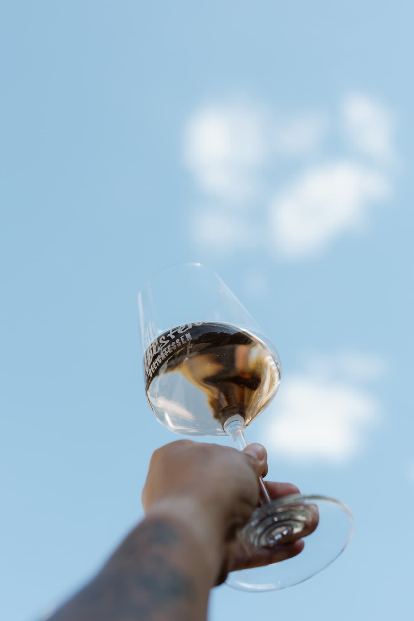 Ein Glas Roséwein wird gegen den blauen Sommerhimmel gehalten